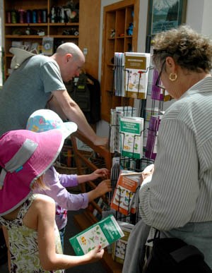 Two girls, a woman, and a bear look at items in a small store