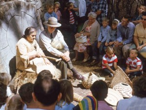 A woman in American Indian clothing gives a demonstration to a group of people.
