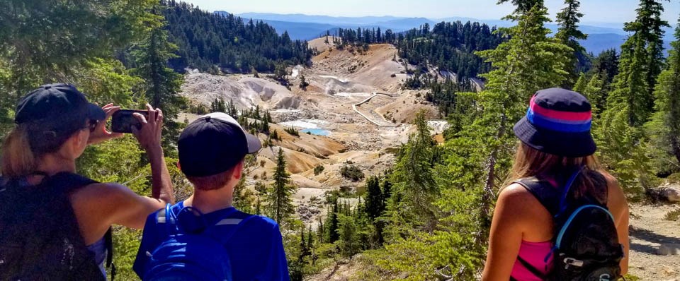 Two kids and a woman look down into a hydrothermal area