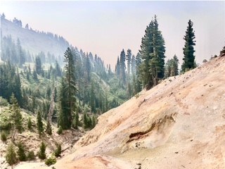 A hazy view of a mudpot on a hillside backed by a windy mountain road.