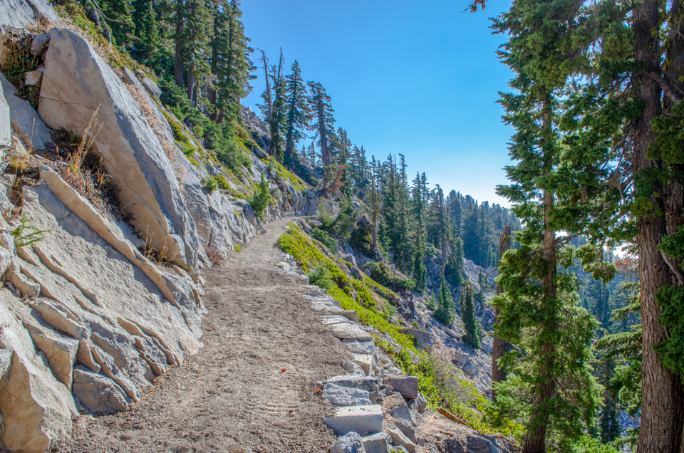 A smooth trail lined by retaining rocks curves along a steep hillside