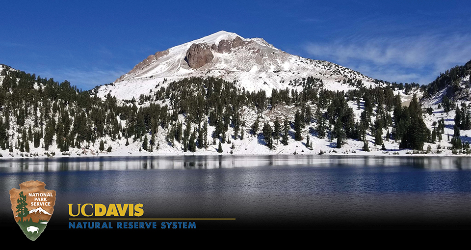 A snow-covered mountain above a blue lake with an arrowhead logo at bottom and another logo that reads "UC Davis Natural Reserve System"