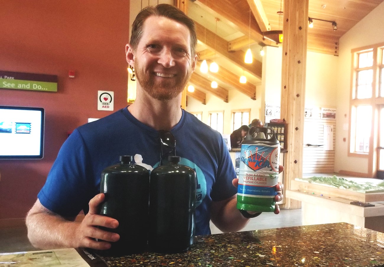 A man holds three propane canisters at a standing counter