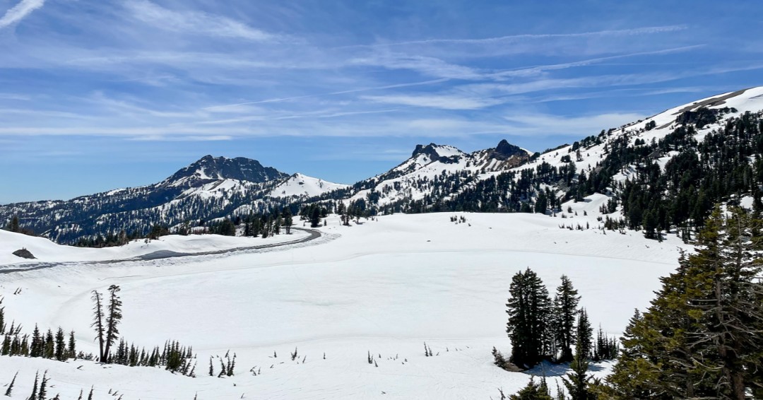 Lake Helen covered with a blanket of snow. Snow-covered peaks in the background and a cleared highway.