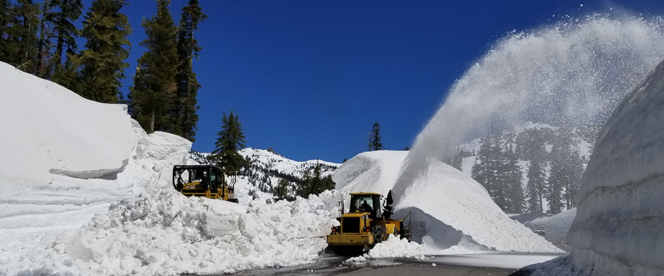 A bulldozer and rotary plow clear snow from a road