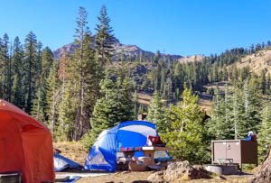 A blue shade structure and orange tent at the base of a jagged mountain peak.