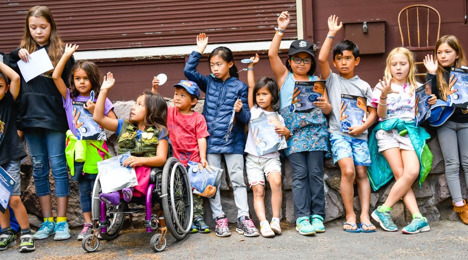 A group of kids stand with hands raised at a program about exploring the night sky