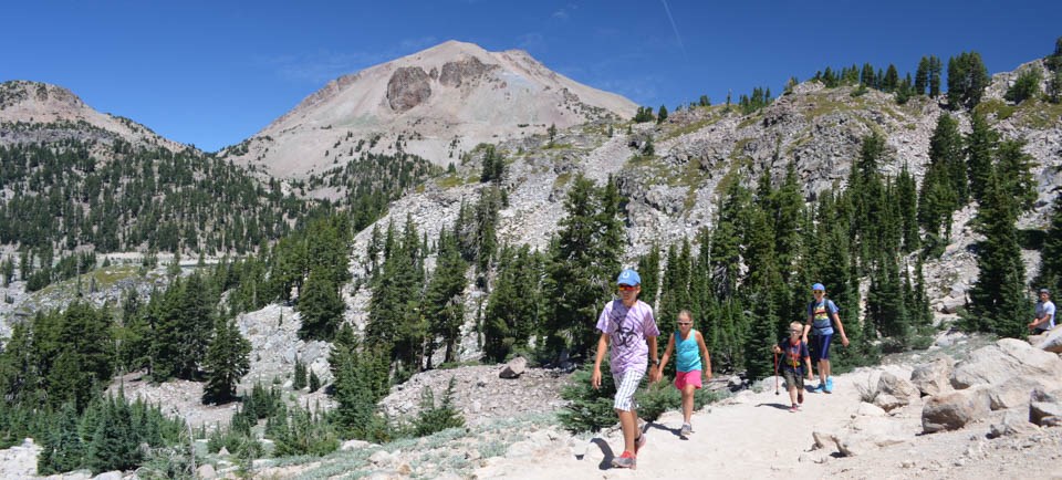 Four kids hiking on a trail backed by a large volcano.