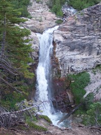 A view looking down on Mill Creek Falls surrounded by volcanic rock and trees.