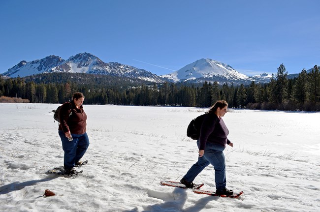 two snowshoers in an open snowy area, mountain in background