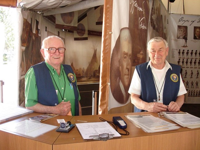 Two male volunteers working behind an information desk.