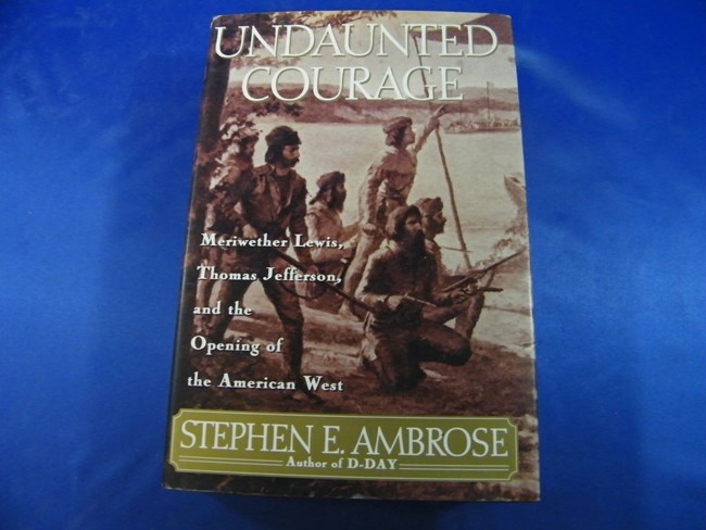 1734 (1) A copy of the first edition of “Undaunted Courage,” released in 1996. The front cover features a monotone illustration of several members of the Corps of Discovery overlooking a river. The title is set in a large, white font across the top and across th