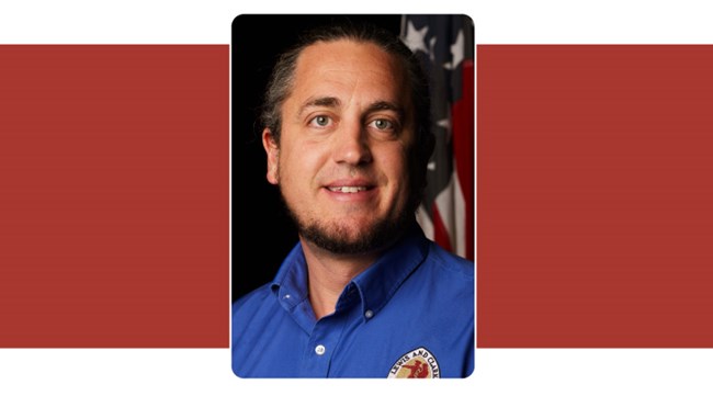 Portrait of man with hair pulled back and wearing shirt and tie. American Flag background.