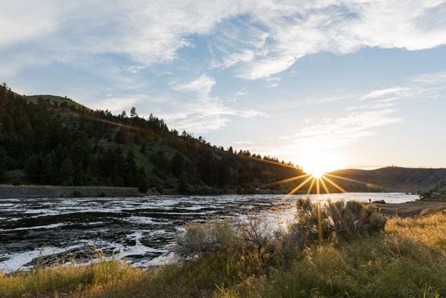 sun setting over a river and hills