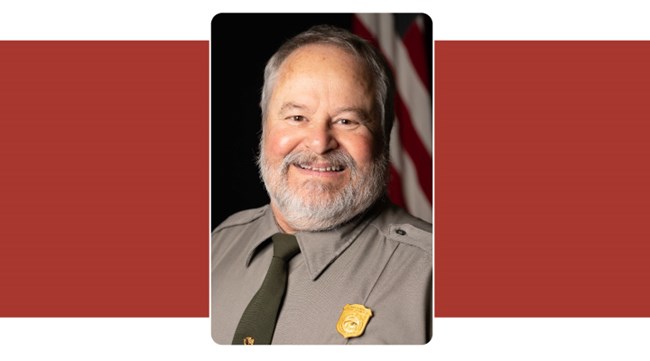 portrait of man with white beard. American flag in background.