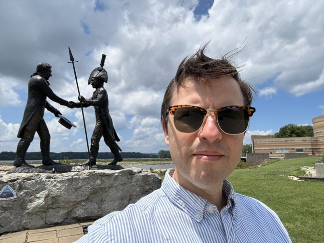 a man in sunglasses stands in front of a statue of two mean shaking hands