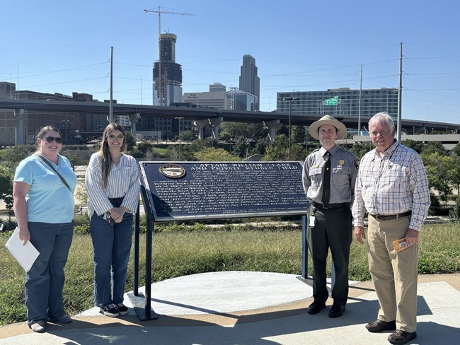 four people stand near a sign outdoors