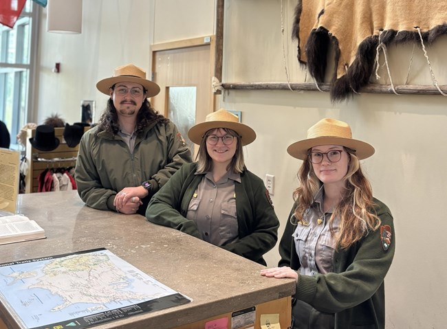 three people in park ranger uniforms stand at a desk