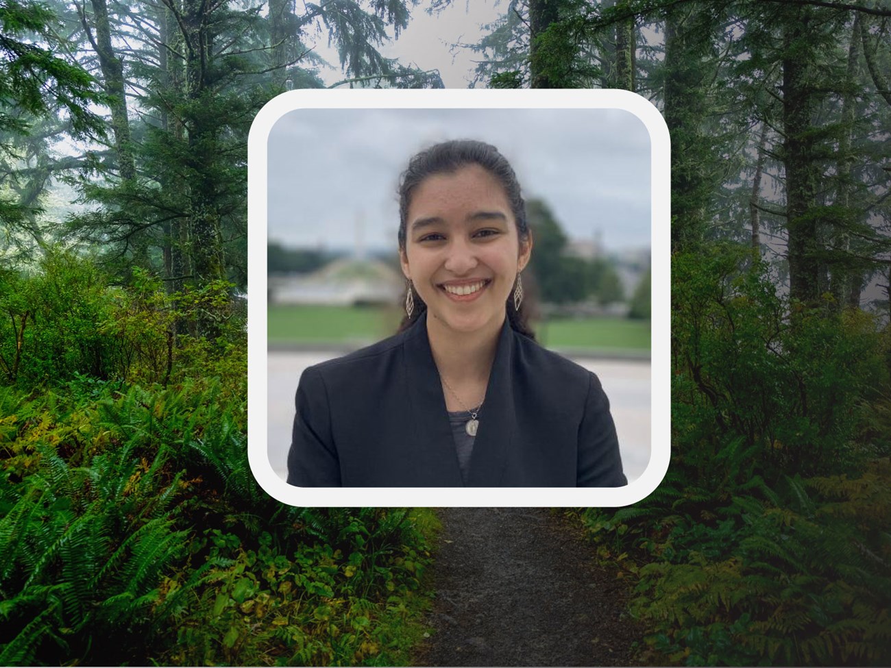 Photo of young woman in a blazer. A path of evergreen trees behind