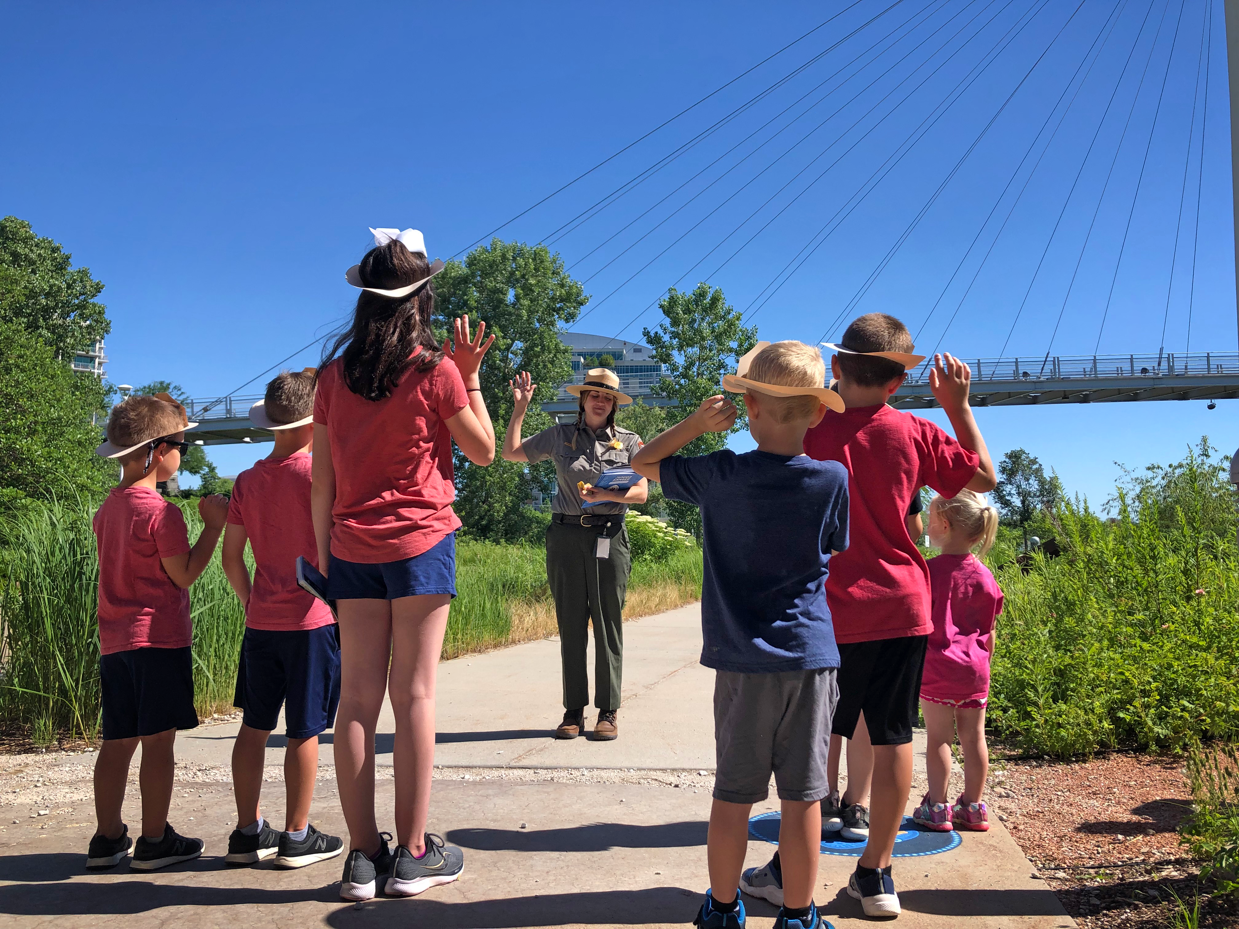 Junior Rangers at Lewis and Clark Trail Headquarters Visitor Center-2021 Ranger leads group of children in Junior Ranger Pledge. All stand wit their right hands raised. Bridge in background