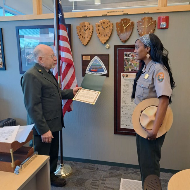 Kassey-Trahanas-Lewis-and-Clark-Trail-2022 Two National Park Service rangers face each other. A man hands a young woman a certificate.