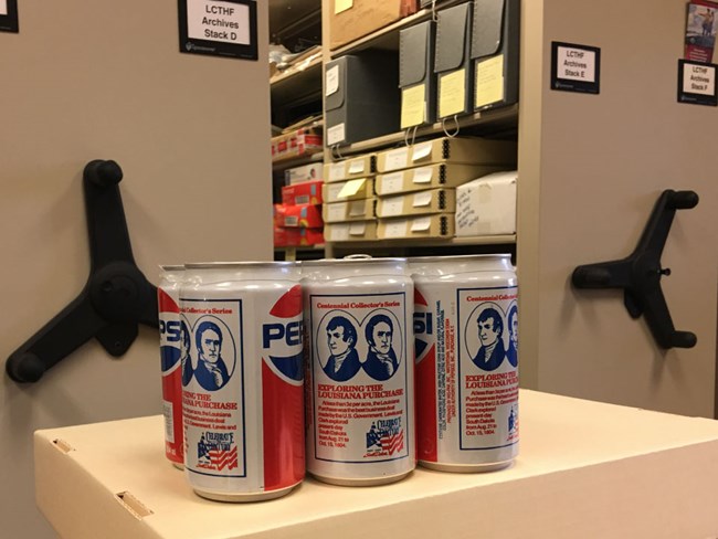 In an archive room with rolling shells, a sits a vintage 6 pack of Pepsi cans with Lewis and Clark's portraits.