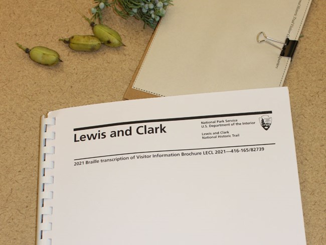 Photo of Braille edition of Lewis and Clark Trail brochure. White spiral bound notebook with braille transcription.