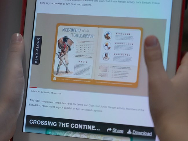 Lewis-and-Clark-Trail-Junior-Ranger-Read-Along-in-action Photo of child holding tablet. A video is on the screen. A historic activity booklet page is featured.