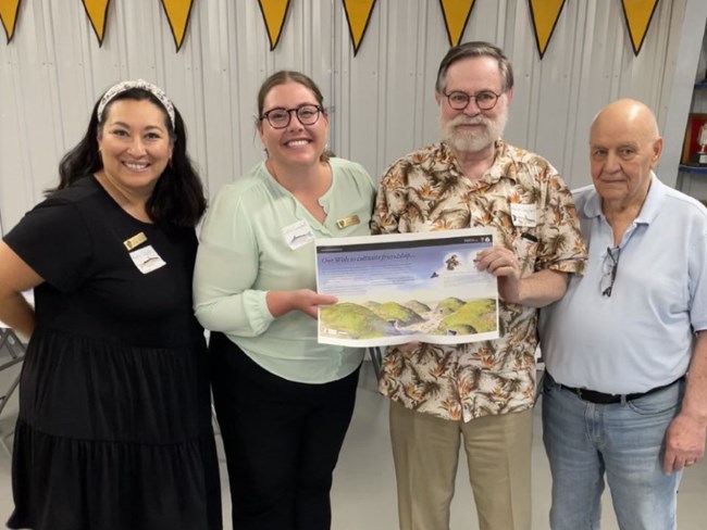 Four people pose, holding a printed out design of a wayside panel.