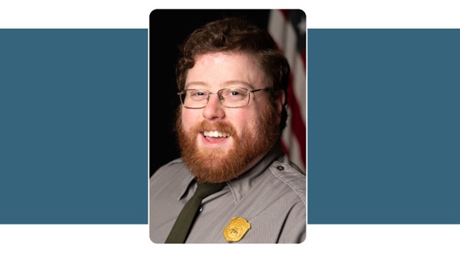 portrait of man in Park Service Uniform, glasses, and with reddish hair and beard. American flag background