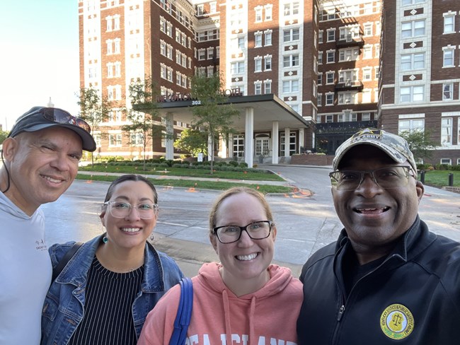four people smile in front of a building