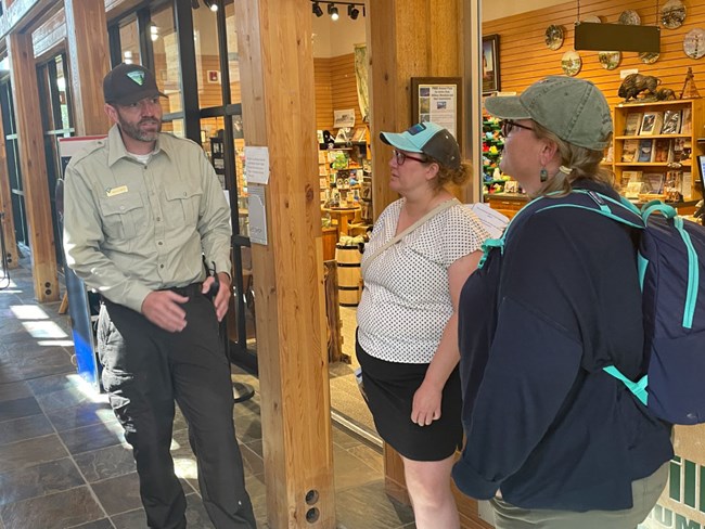 A male park ranger talks with two women inside a visitor center. The Ranger wears a Bureau of Land Management uniform.