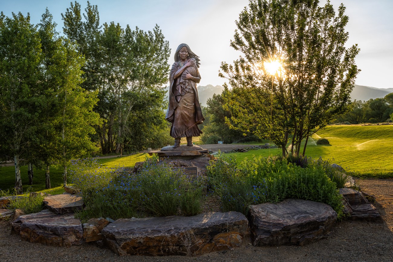 a bronze statue of a Native woman surrounded by plants