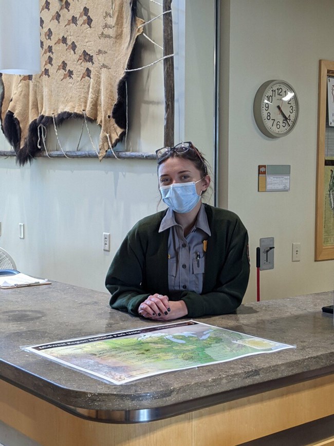 Ranger wearing mask sits behind visitor center desk