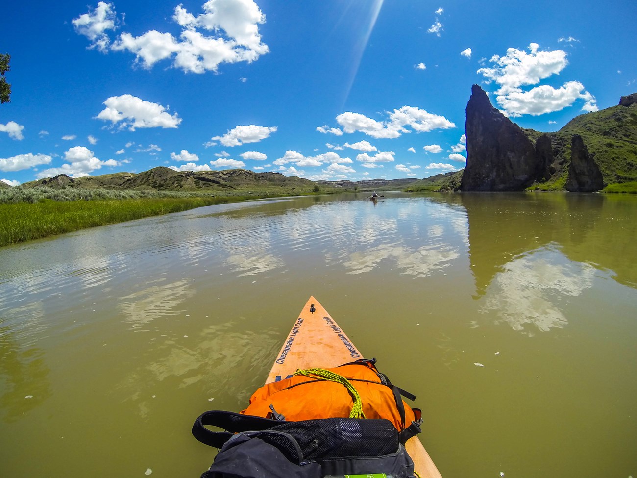 the front of a kayak on a river with a clear sky behind