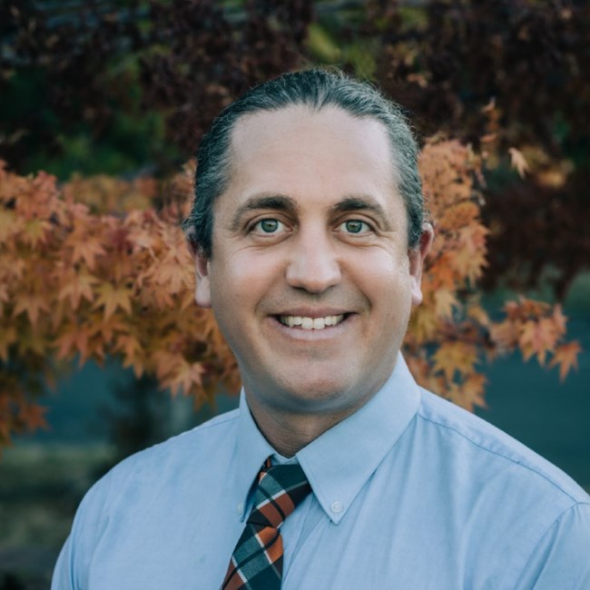 Portrait of person in shirt and tie, hair pulled back.