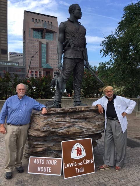 Easter-Extension_Digital-Annual-Report-2021 Two men pose with Lewis and Clark Trail Auto Tour Route Signs. Decorative tab reads Partner. Tan background.
