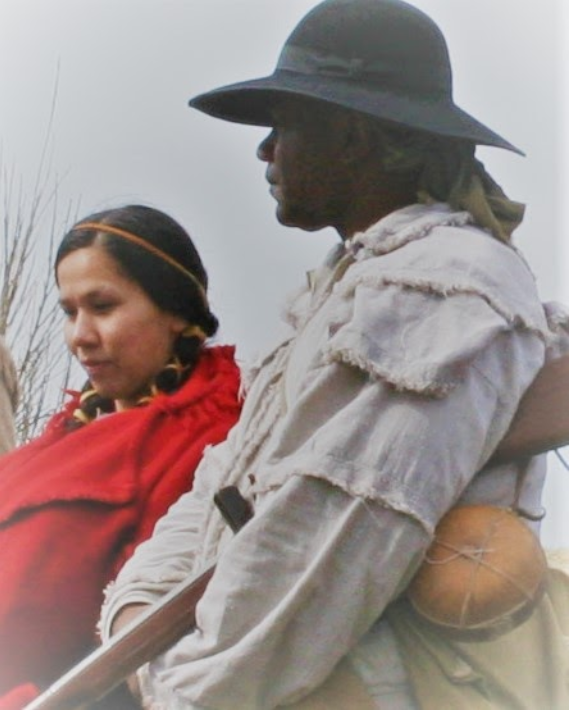 A woman and man depicting Sacagawea and York standing side by side wearing canvas and cloth with a musket in hand