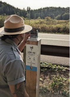 A ranger in grey uniform and tan flat hat sets up a cell phone on the chronolog photo station overlooking the tidal wetlands