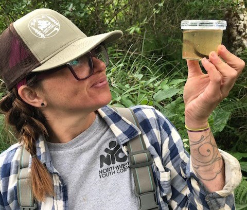 An intern holds up a small plastic container with a dragonfly larvae specimen as she turns to look at it.