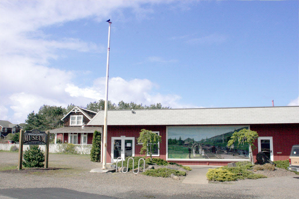 A red onestory building with a white roof featuring a picture and sign reading the Seaside Museum and Historical Society