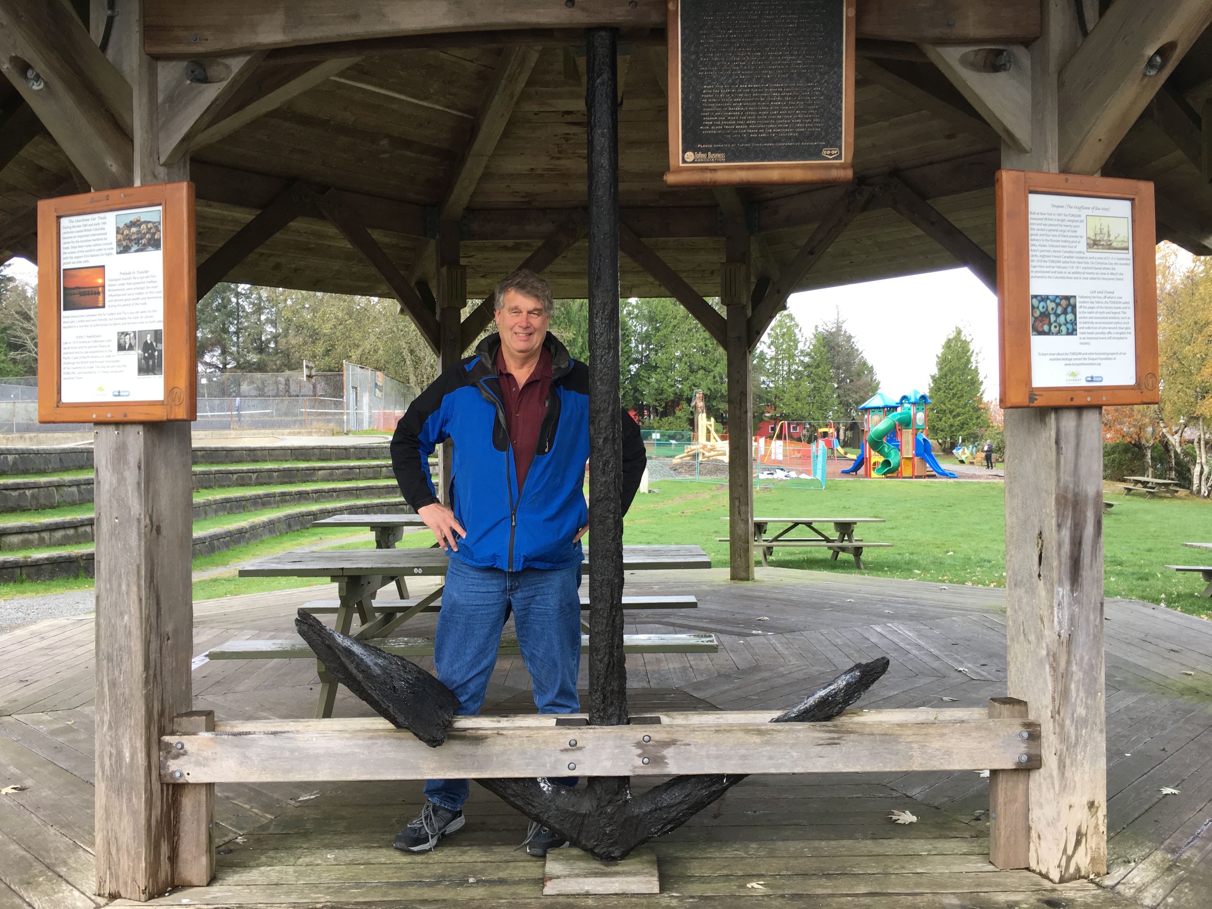 A man in a blue rain jacket stands next to a metal anchor that is approximately 10 feet tall.