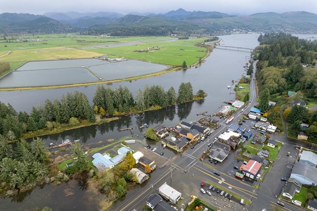 Aireal view of a flooded community. The Nehalem river in the center of the picture with water in fields and in parking lots surrounding houses and stores.