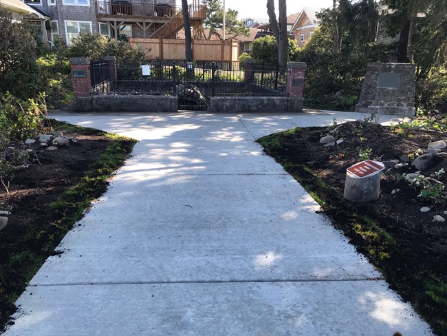 Sidewalk leading up to a rectangular space with a recreation of a saltwork surrounded by a short brick wall and iron bar fence.