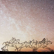 Sculpture of Indians on horses at night with start trails