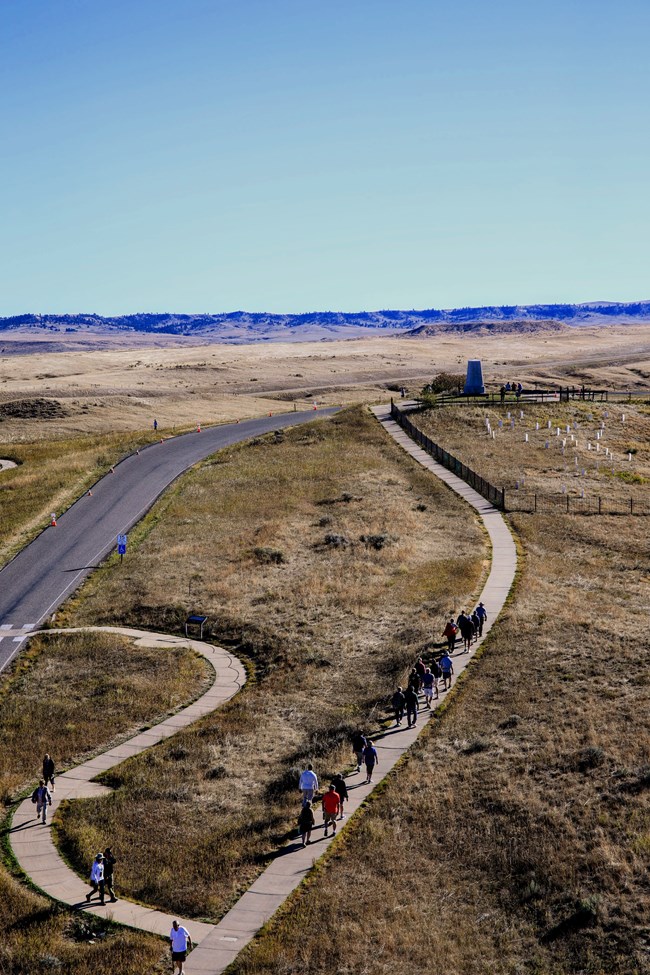 Visitors walk up a paved path to a monument.