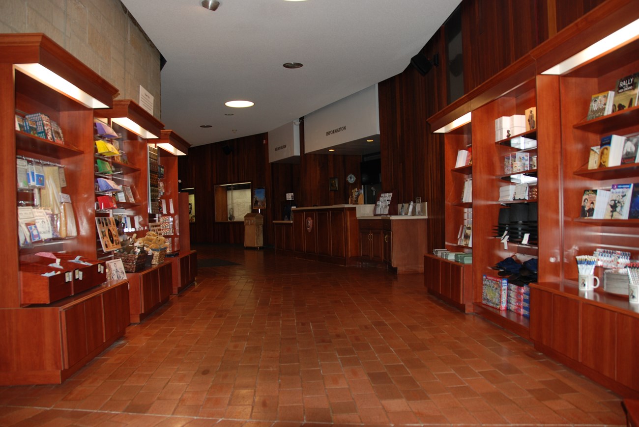 Six bookshelves on both sides of aisle filled with books, games, toys, and other sale items. Information desk and entrance to auditorium in back.