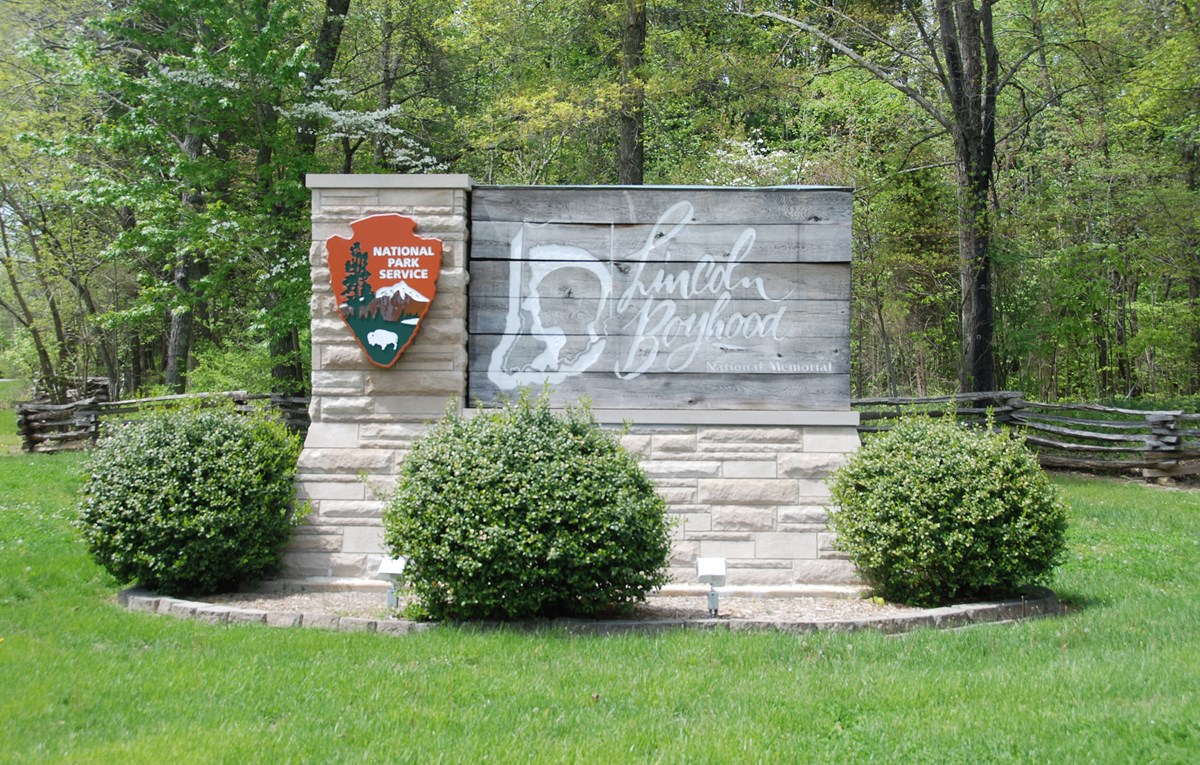 wooden park entrance sign with split-rail fence and trees