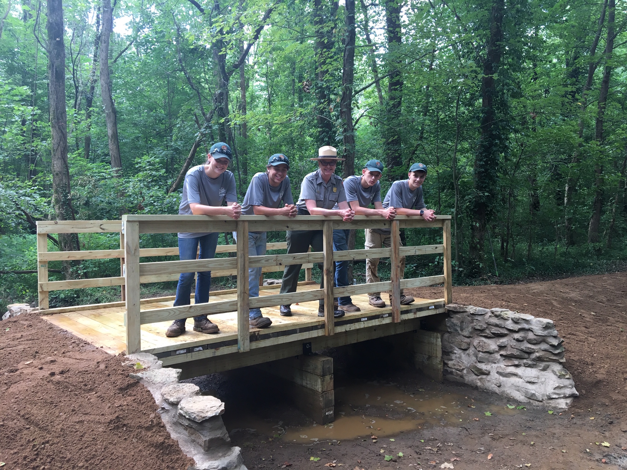 Park Ranger with four workers leaning on railing on bridge.