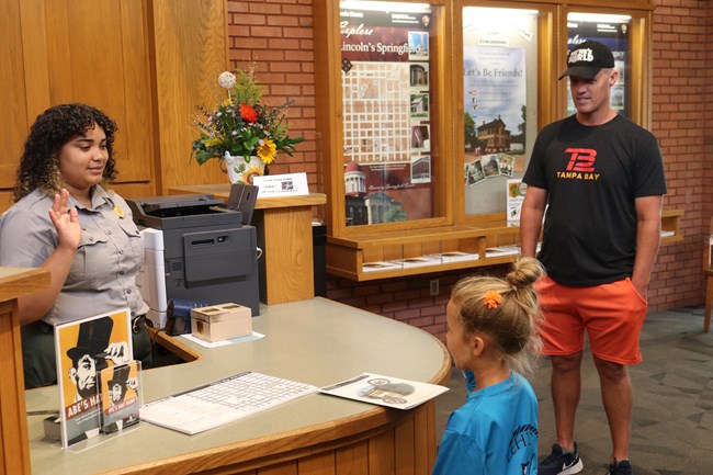 A ranger swears in a junior ranger at a desk